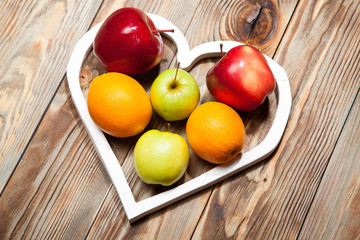 White heart, apples and oranges on the wooden background
