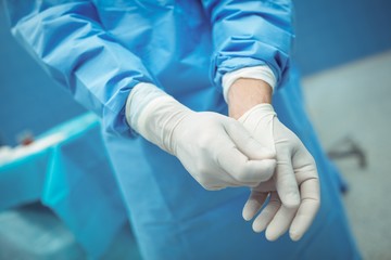 Male surgeon removing surgical gloves in operation theater - Powered by Adobe