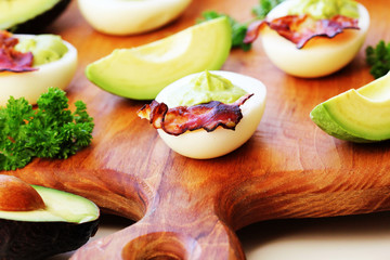 deviled eggs with avocado and bacon on cutting board