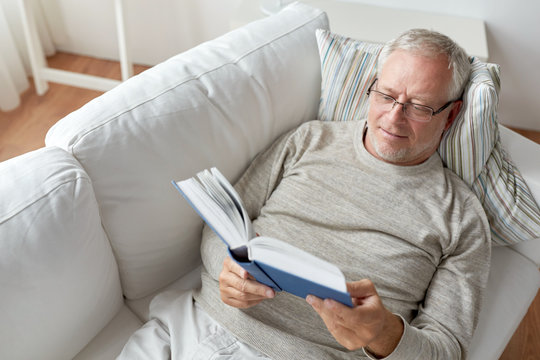 senior man lying on sofa and reading book at home