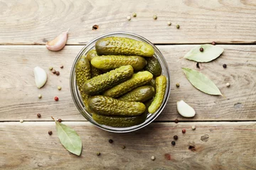 Poster Pickled gherkins or cucumbers in bowl on wooden rustic table from above. © juliasudnitskaya