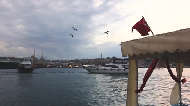 Turkish flag waving over a boat in Istanbul. Galata bridge is on the left side of the frame, and there are some mosques on background