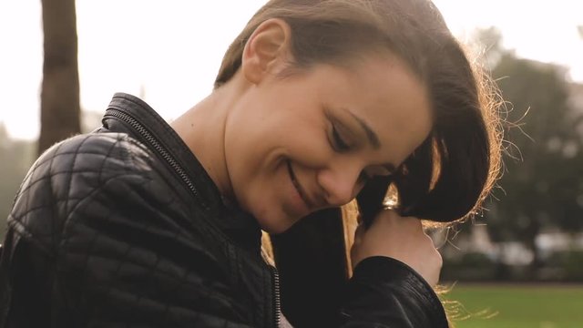 Girl making a braid with hair at park. Young woman alone taking care of the hair. Backlight technique with real flare.