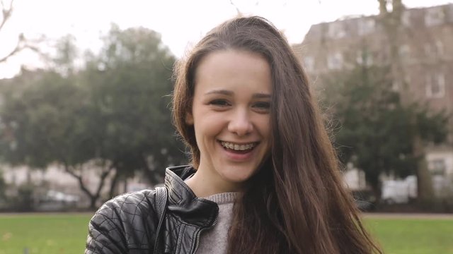 Girl portrait at park. Young woman alone at park in London, looking at camera and around, smiling and making faces. Slow motion