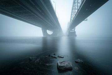 Two parallel bridges over foggy river and stones in the water on foreground.. Long exposure shot.