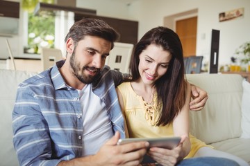 Happy couple using digital tablet while relaxing on sofa