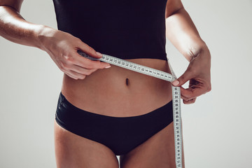 Athletic slim woman measuring her waist by measure tape on white background