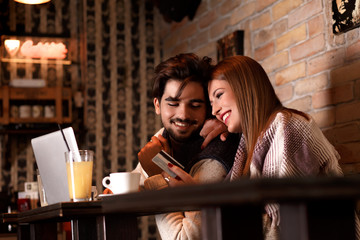 Beautiful young couple with laptop in cafe, they are shopping on line with credit card.