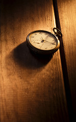 Fototapeta na wymiar Vintage pocket watch with shadow on wooden background under beam of light