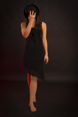 Beauty low key portrait of a young brunette woman with hat that cover face. Red backlight, black background