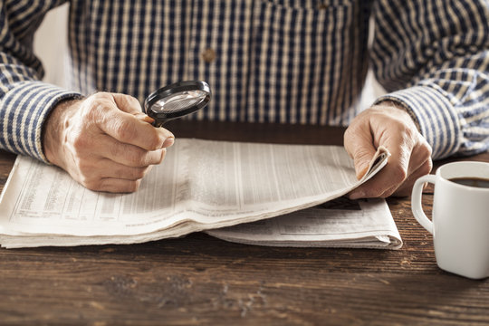 Man reading newspaper with magnifying