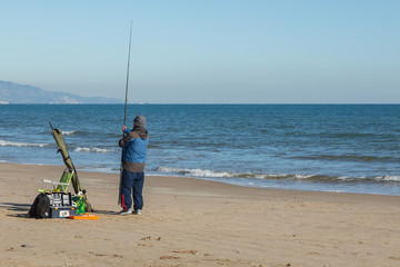 Man fiskar med kastspö på en sandstrand vid havet