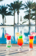 Colored cocktails on a background of water. Colorful cocktails near the pool. Beach party. Summer drinks. Exotic drinks. Glasses of cocktails on table near pool. Summer drinks photo concept. Сocktail