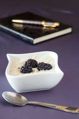 Healthy oatmeal with dried fruit and blackberry, blurred notebook and pen on back background