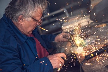 Mature male worker grinding metal in workshop