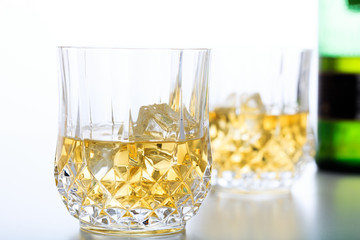 Glasses of whiskey and ice on white background