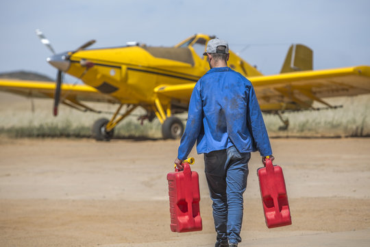 Mechanic carrying jerry cans towards yellow crop dusting plane