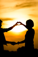 Silhouette of happy young couple outdoors making  heart shape 