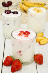 Strawberry, banana and cherry yogurt on a white wooden background. Healthy diet