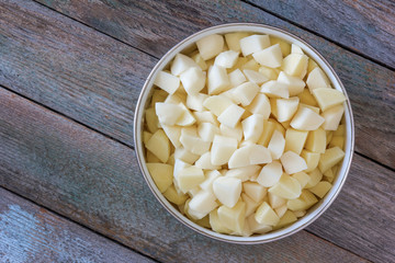 sliced pieces of raw potatoes in a circular bowl on an old rustic wooden table. top view closeup