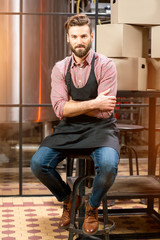 Full body portrait of a handsome brewer in apron and checkered shirt at the manufacturing