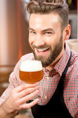 Fototapeta premium Close-up portrait of handsome brewer tasting beer in the glass