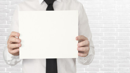 A young business man in the office with a tie holding an empty card with copy space. Wall background.