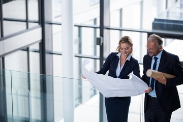 Business colleagues discussing with blueprint in corridor
