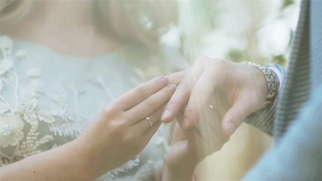 Woman putting ring on mans finger close up through veil or sun light. Girlfriend proposing to girlfriend as gender equality concept. Exchanging wedding rings at ceremony in nature outdoors