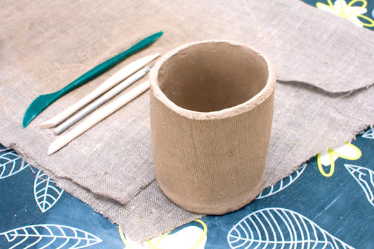 Just Finished Cup Made of Raw Clay with sculpt Tools on Sackcloth as Background on Workshop Table