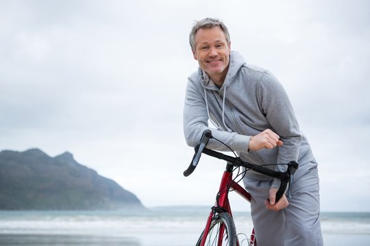 Portrait Of Happy Man Leaning On Bicycle At Beach