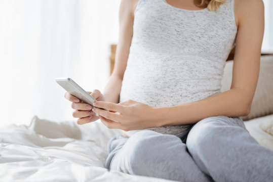 Close up of a pregnant woman using smartphone in bedroom