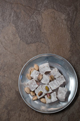 Turkish dessert with pistachios on a vintage pewter plate. Brown natural stone background. Copy space. 