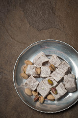 Turkish dessert with pistachios on a vintage pewter plate. Brown natural stone background. Copy space. 