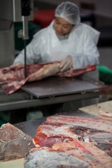 Female butcher cutting raw meat on a band saw machine