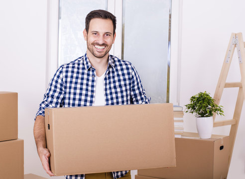 Young smiling man holding cardboard box and moving into new home. 