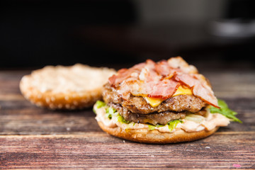 Tasty grilled beef burger with lettuce, ketchup, onion rings, chili and mayonnaise served on pieces of brown paper on a rustic wooden table of counter, with copyspace