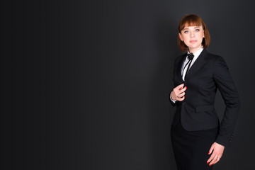 Cheerful confident business woman standing in dark office room and looking at camera. Charming businesswoman on black background with copyspace for your text.