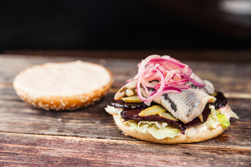Tasty grilled beef burger with lettuce, ketchup, onion rings, chili and mayonnaise served on pieces of brown paper on a rustic wooden table of counter, with copyspace