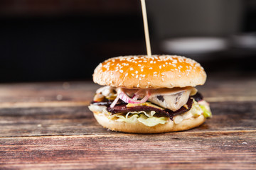 Tasty grilled beef burger with lettuce, ketchup, onion rings, chili and mayonnaise served on pieces of brown paper on a rustic wooden table of counter, with copyspace