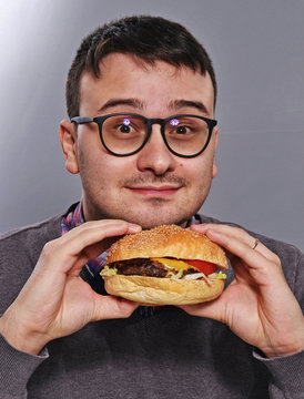 Retrato de un joven nerd con anteojos comiendo hamburguesa.