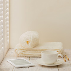 Knitting, e-book and a cup on a light wooden background near a w