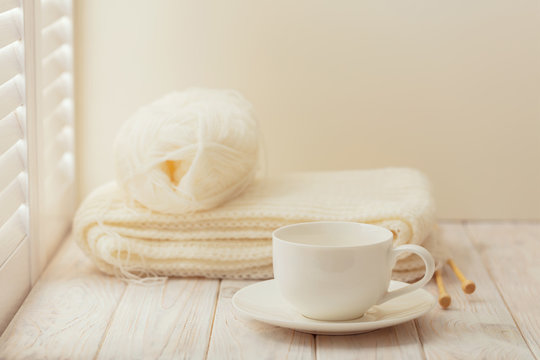 Knitting and a cup on a light wooden background near a window wi