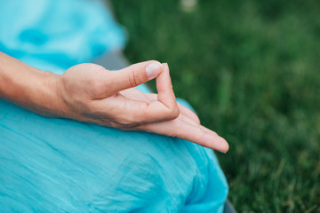 Woman meditating in lotus position closeup. Hands close-up mudra. Sitting on rug the lawn of green...