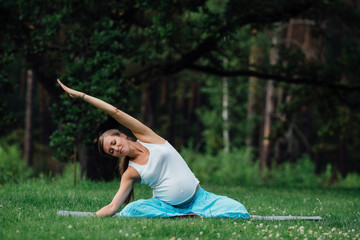 pregnant yoga in the lotus position on the forest background. in the park the grass mat, outdoor, health woman.