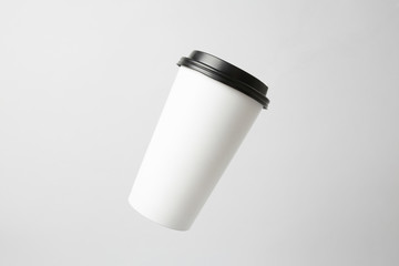 Blank white paper cup with a black cap in the air