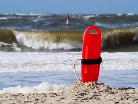 Red flotation device (buoy) for water rescue at the beach. Windy day at the north sea.