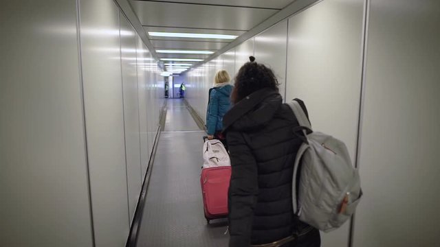 Airport. Two young women running on your flight. Blonde girl with a suitcase in a hurry to pass through the pipe to the plane. Brunette with a backpack on his shoulders in a great mood.