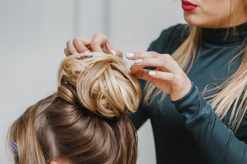 Hairdresser makes upper bun hairstyle close-up on brown hair of beautiful woman