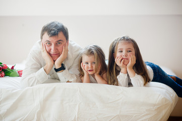 The young father and two of his charming little daughters lie on a bed.